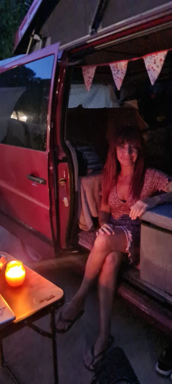 Escena nocturna de Júlia i Scarlett. Júlia està asseguda a la part de darrere de la furgoneta, amb la porta oberta les cames  fora. Porta un vestit vermell, el cabell és vermell, Scarlett és vermella, hi ha una espelma encesa damunt d'una taula.